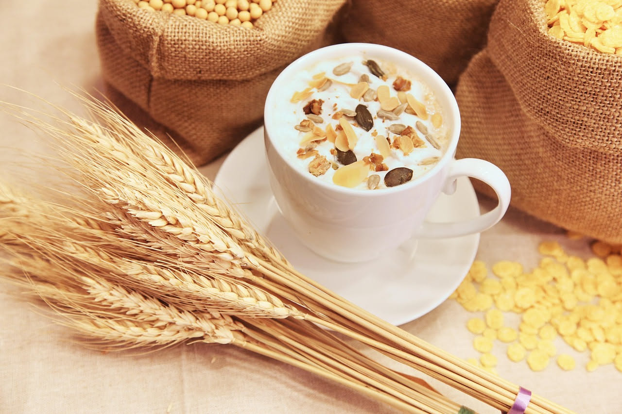 Ciotola in ceramica con chicchi di orzo, farro e avena sfusi, accanto a spighe di grano intero su una superficie di legno rustico