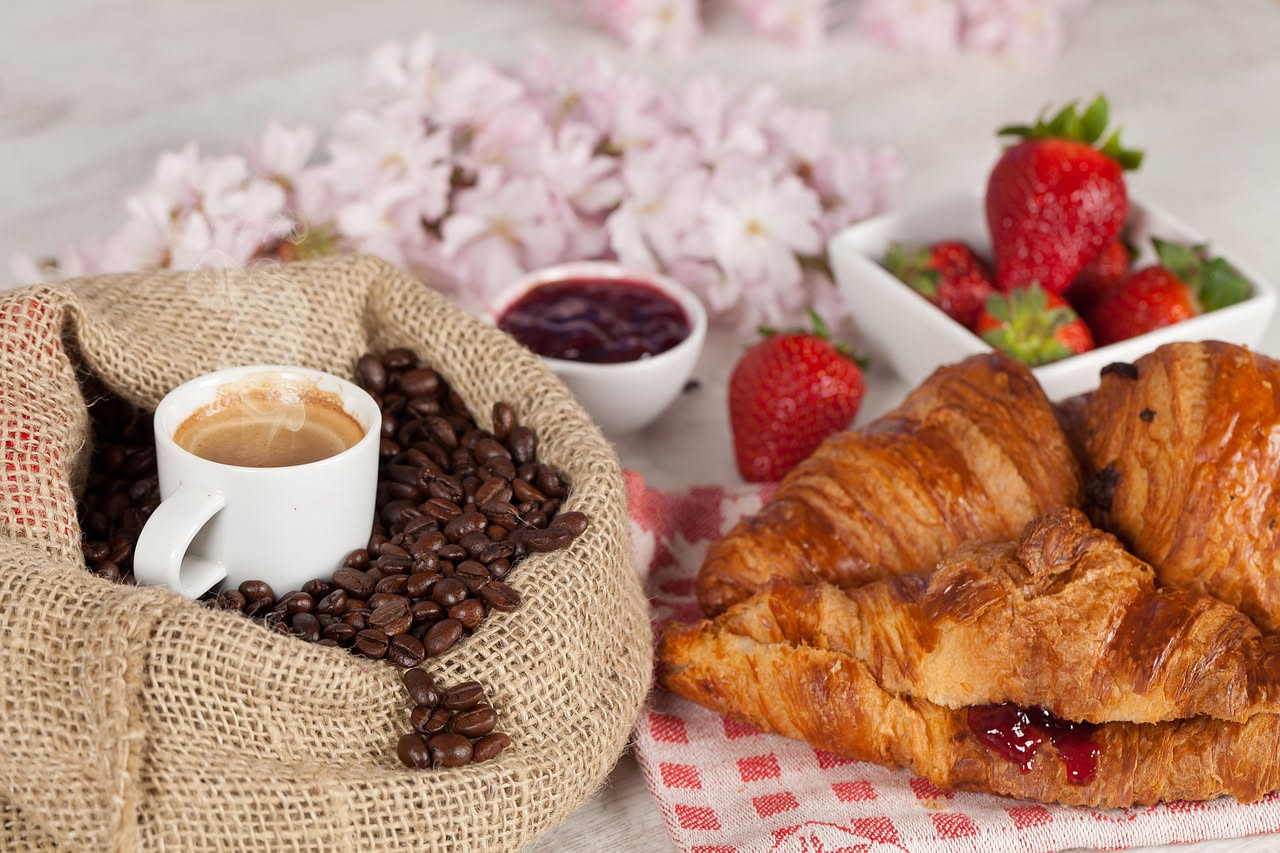 Tavolo da colazione con uova strapazzate, pane integrale tostato, fragole fresche, miele e una tazza di caffè su sfondo di luce naturale primaverile