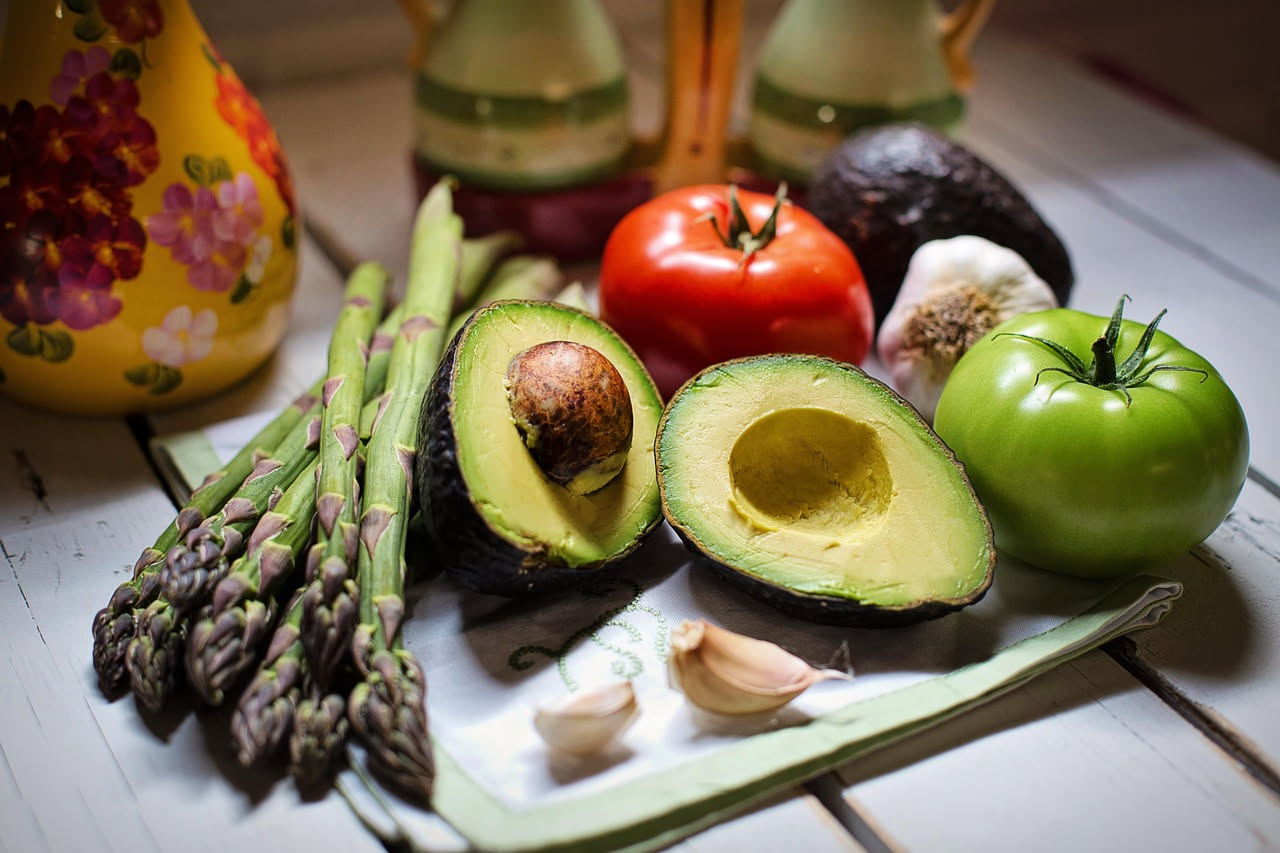 Tavolo con verdure verdi fresche di primavera, asparagi, spinaci, insalata, pane integrale, pesce azzurro e limoni su superficie bianca