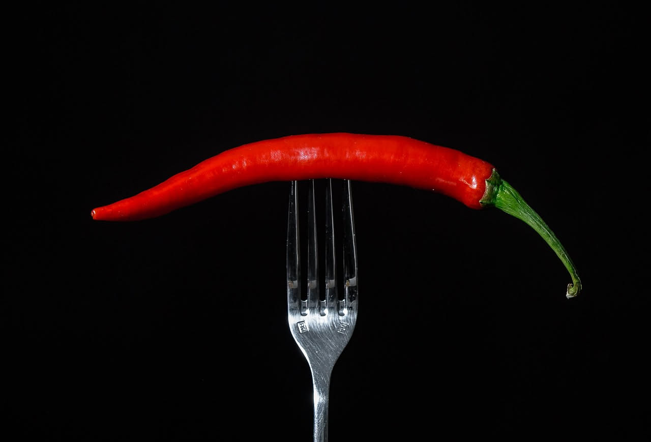 Peperoncini rossi, gialli e verdi freschi disposti su un tagliere di legno, con alcuni peperoni interi e uno tagliato a metà per mostrare i semi all'interno