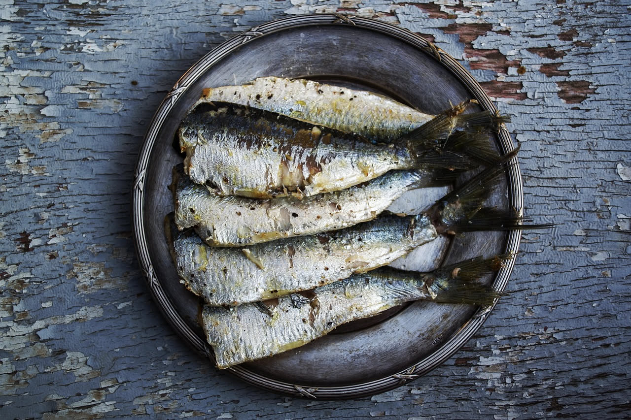 Sardine e acciughe fresche in un piatto bianco con limone fresco tagliato a fette e olio d'oliva