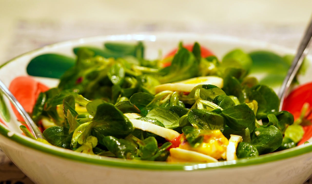 Insalata fresca con lattuga, pomodori e verdure colorate in una ciotola trasparente con un filo di olio d'oliva versato da una bottiglia
