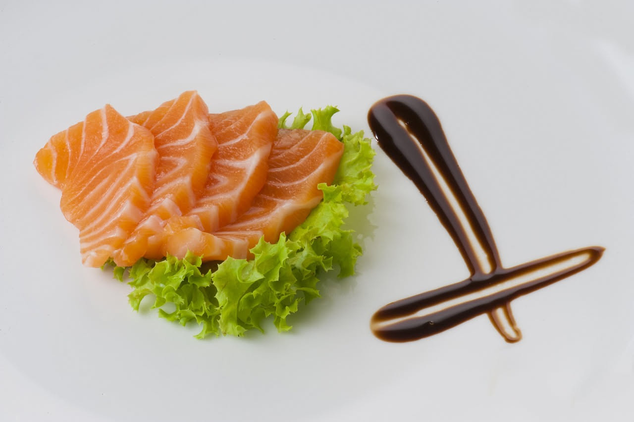 Piatto di carpaccio di pesce fresco con limone, erbe aromatiche e olio extravergine, servito su un tavolo esterno in ombra durante l'estate