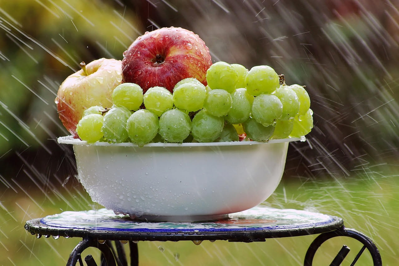 Mani che lavano pomodori rossi sotto acqua corrente, con gocce trasparenti e sfondo di verdure fresche colorate