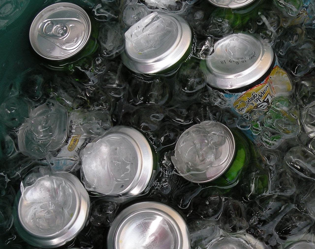 Bicchiere di birra ghiacciata con gocce di condensa su sfondo estivo con sole, mare e sabbia bianca