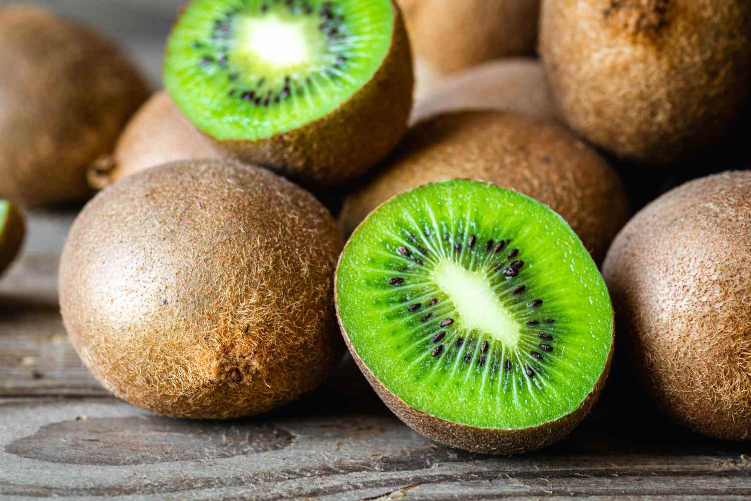 Due kiwi tagliati a metà su un piattino bianco accanto a un cucchiaino, posati su un comodino di legno illuminato da luce calda serale.